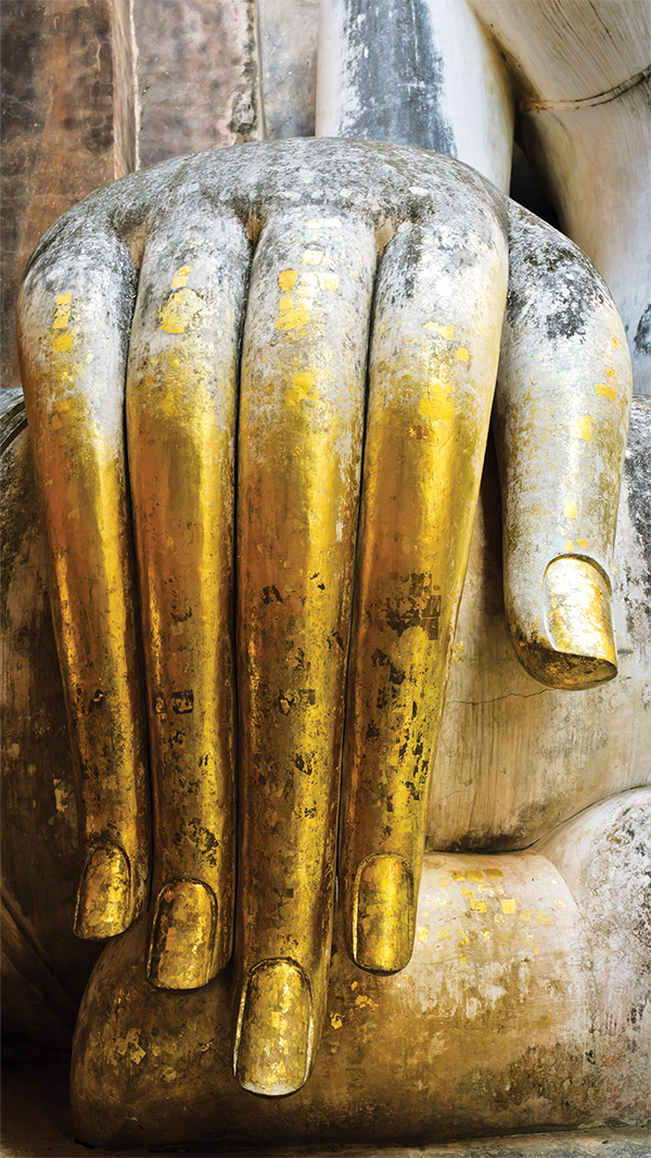 Gold-leafed hand of an ancient Buddha statue, symbolizing traditional Thai healing heritage